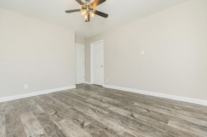 A spacious, empty room featuring a light-colored wall, a ceiling fan with four bulbs, and laminate flooring. Two white doors are visible on the left side, one leading to a closet. The overall atmosphere is bright and airy, ideal for various decor styles.