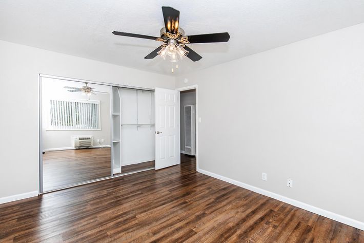 Interior view of a room featuring light grey walls and a fan with a chandelier-style light fixture. There are two open white doors leading to a closet and another room, and the floor is covered in a wood-like laminate.