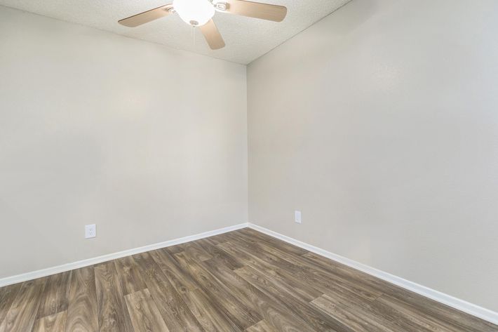 A minimalist interior space with light-colored walls and a smooth wooden floor. A ceiling fan with light is visible, and the room has no furniture, emphasizing an open and airy feel. The absence of decorations gives it a simple, clean aesthetic suitable for various purposes.