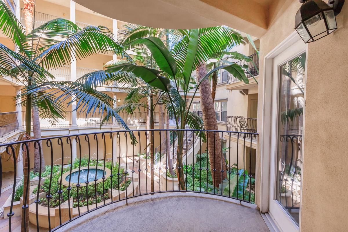A balcony view overlooking a landscaped courtyard with tropical plants and a circular fountain, surrounded by building structures.