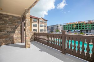 A balcony view overlooking a swimming pool with landscaped surroundings, featuring a stone railing. In the background, there are multi-story apartment buildings and ongoing construction of additional structures under a clear blue sky.
