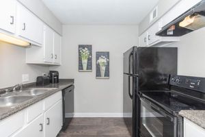 A modern kitchen featuring white cabinetry, a granite countertop, and stainless steel appliances. It includes a black refrigerator, black stove, and a dishwasher. The walls are light gray, and two framed pictures of flowers hang above the sink. Soft lighting illuminates the space, creating a welcoming atmosphere.