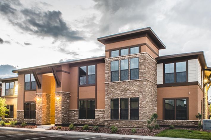 Modern two-story building with a mix of stone and stucco exterior, featuring large windows and a warm color palette, set against a cloudy sky.