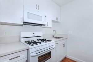 A modern kitchen featuring white cabinetry, a gas stove with an oven, a microwave above it, and a stainless steel sink. The countertops are light-colored, and the walls are painted in a neutral tone, creating a clean and bright appearance.