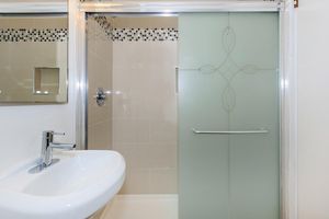A modern bathroom featuring a sleek shower enclosure with frosted glass, a stylish sink with a contemporary faucet, and tiled walls. The design includes decorative tile accents and a minimalist mirror, creating a clean and elegant aesthetic.