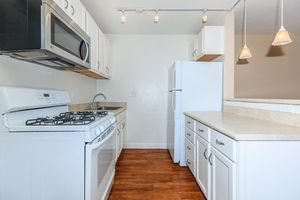 Modern kitchen featuring white cabinetry, a gas stove, microwave, and a spacious counter. There is a refrigerator and pendant lighting above the counter. The flooring is hardwood, creating a warm and inviting atmosphere.