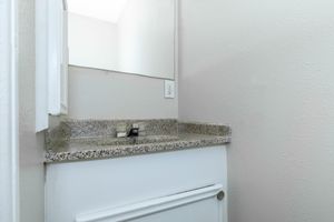 A small bathroom sink area featuring a granite countertop, a faucet, and a mirror on the wall. The walls are painted in a light color, and the space is well-lit, creating a clean and minimalistic appearance.