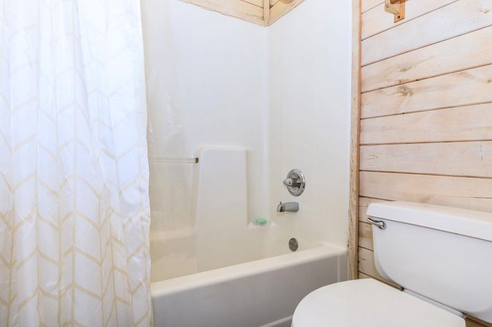 A clean bathroom featuring a tub and shower combination. The white shower curtain has a geometric pattern. The walls are wooden, and there is a toilet positioned beside the tub. The overall atmosphere is bright and well-maintained.