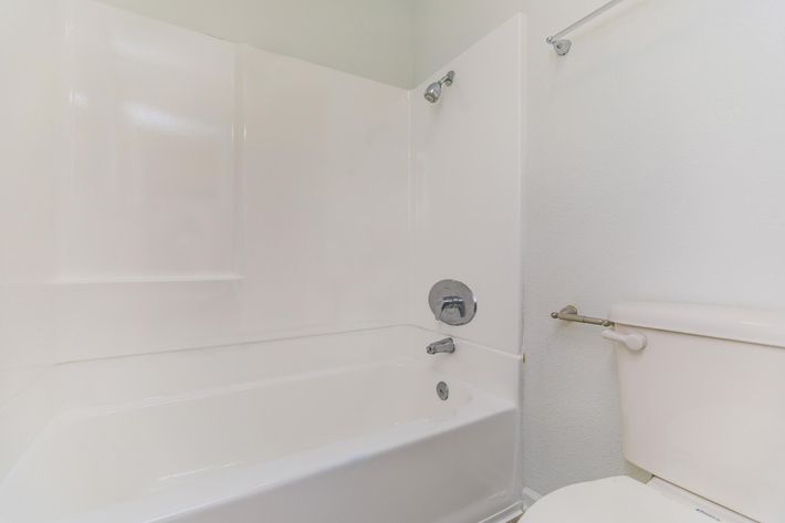 A clean, modern bathroom featuring a white bathtub with a shower head, a chrome faucet, and a white toilet. The walls are light-colored, and the space is well-lit, creating a fresh and airy atmosphere.