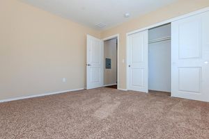 A spacious, empty room with light beige walls and a beige carpet. Two white doors lead to a closet and another space. The room has soft, natural lighting, creating a warm and inviting atmosphere.