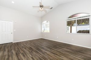 A spacious, empty room with high ceilings and a ceiling fan. There are two arched windows allowing natural light to enter, and the floor is covered with wooden laminate. The walls are painted a light neutral color, creating a bright and airy atmosphere.