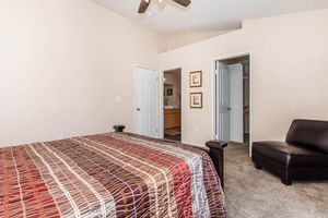 A cozy bedroom featuring a patterned bedspread on a large bed, with a leather chair in the corner. Two doors lead to an adjoining room and a bathroom. The walls are painted in a soft, neutral color, and the room has a ceiling fan, creating a comfortable, inviting atmosphere.