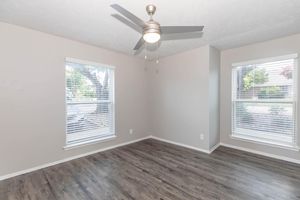 A light and airy room featuring two windows with blinds, a ceiling fan, and wooden flooring. The walls are painted in a neutral tone, and there are no visible furnishings, creating an open and spacious feel.