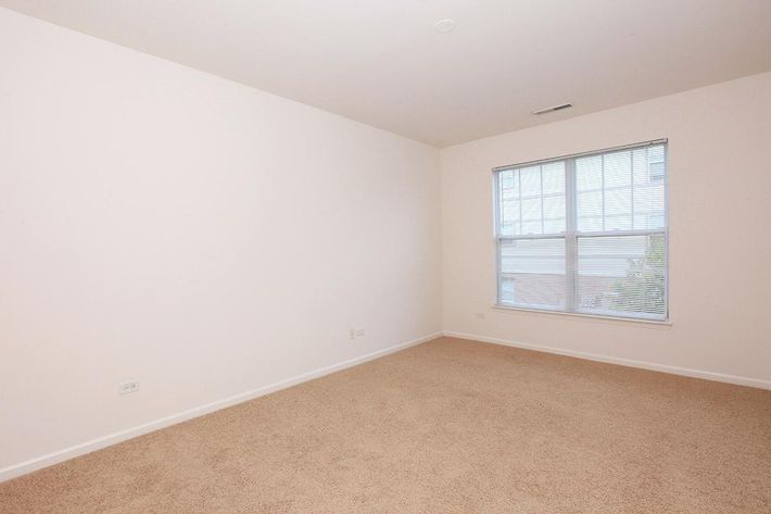 Empty room with beige carpet and white walls. A window with blinds allows natural light to enter. The space appears bright and minimalist, suitable for various uses or furnishings.
