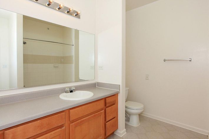 A clean, modern bathroom featuring a large mirror above a sink with a light fixture, wooden cabinetry, and a toilet. The layout includes a tub and shower area, with neutral-colored walls and flooring, creating a bright and spacious atmosphere.