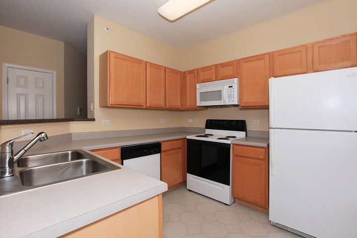 Modern kitchen featuring light wooden cabinetry, a white refrigerator, a black stove and oven, a microwave above the stove, and a stainless steel sink. The countertop is light-colored and there is a dishwasher adjacent to the sink. The walls are painted a soft yellow, enhancing the open feel of the space.