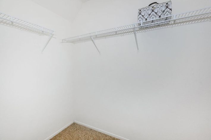 A sparsely decorated empty closet with white walls and a light-colored floor. The closet features wire shelving along the upper walls, and a decorative storage box sits on the shelf in the top right corner, creating a minimalistic and organized appearance.