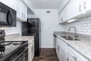 Modern kitchen with white cabinets, granite countertops, and stainless steel appliances, including a black microwave, refrigerator, and oven. The backsplash features white subway tiles, and there is a stainless steel sink with a faucet. The flooring is dark-colored wood. Bright and spacious atmosphere.