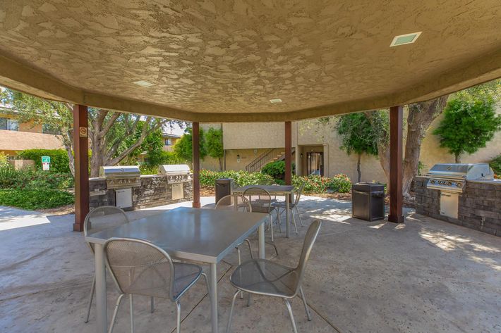 A table and chairs under a pavilion with stainless steel barbecues