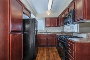A modern kitchen featuring dark wood cabinetry, a black refrigerator, a black gas stove, and a microwave. The countertops are light-colored, and the floor is hardwood. A window provides natural light, and the space is designed in a functional layout with various kitchen appliances.