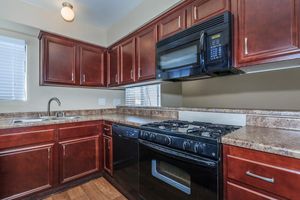 Modern kitchen featuring dark wood cabinetry, granite countertops, a stainless steel sink, and a black gas stove and microwave. Natural light enters through the window with blinds. The overall design combines functionality and style in a cozy environment.