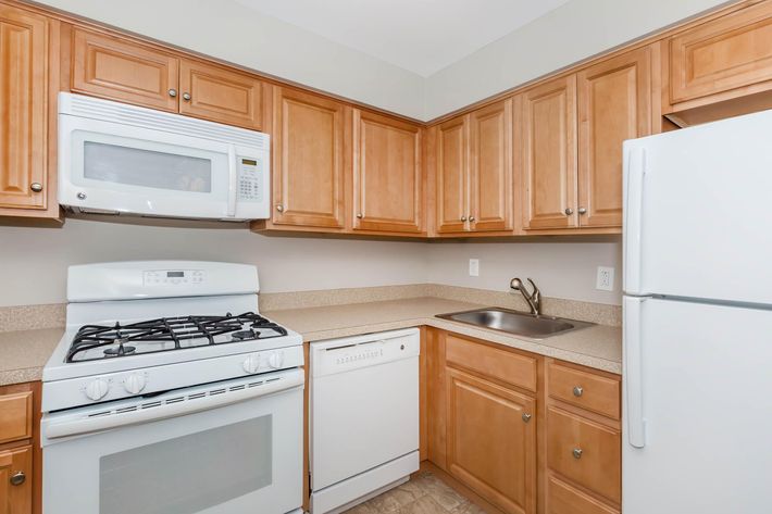 A modern kitchen featuring wooden cabinets, a white gas stove, a built-in microwave, a sink, and a white dishwasher. The countertop is beige and the floor has a light tile design, creating a warm and inviting cooking space.
