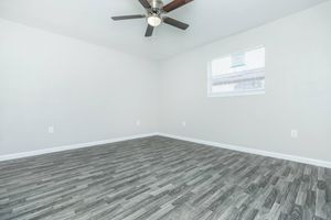 Empty room featuring a light gray wall, wood-like flooring, a ceiling fan with dark blades, and a single window with blinds. The space is bright and uncluttered, ideal for potential furnishing or decoration.