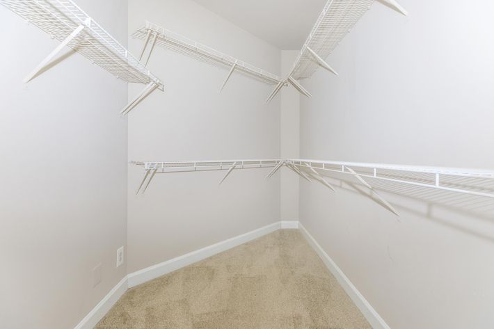 Empty closet space featuring white wire shelving attached to the walls. The room has light-colored walls and a carpeted floor, creating a clean and minimalist appearance. No items are stored on the shelves.