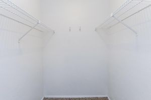 An empty closet with white walls and two wire shelves on opposite sides. The floor is carpeted, and there are two hooks on the back wall. The space is bright and uncluttered, giving a simple and minimalistic appearance.