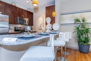 A modern kitchen featuring stainless steel appliances, granite countertops, and stylish white bar stools. A decorative statue and potted plant add elegance to the space, which includes elegant table settings and soft lighting, creating a cozy atmosphere.