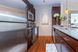 Modern kitchen featuring stainless steel appliances, including a refrigerator and microwave, set against rich wooden cabinets. A granite countertop offers a stylish surface, complemented by a decorative wall art piece and fresh white flowers in a vase. A small rug adds a cozy touch to the hardwood floor.