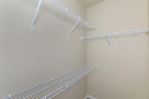 Empty closet with white wire shelving attached to light-colored walls. The shelves are arranged at various heights, providing storage space, and the floor is bare. The overall atmosphere is minimalistic and organized.