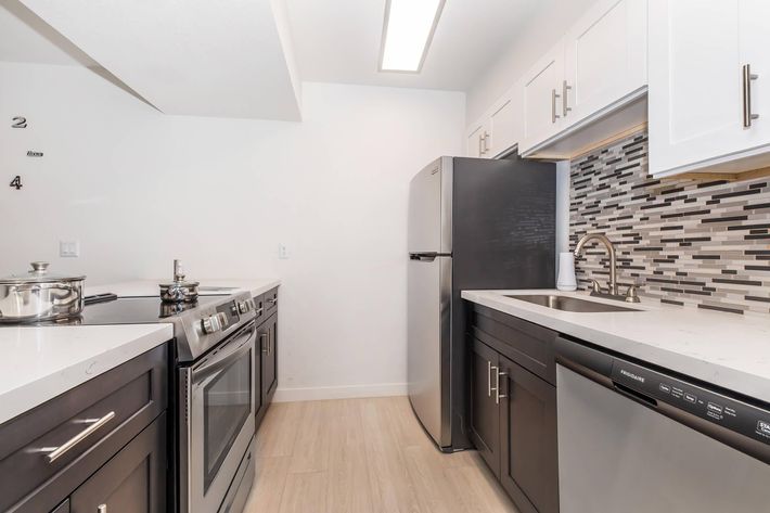 Modern kitchen with stainless steel appliances, including a refrigerator, stove, and dishwasher. The countertops are light-colored with a sleek design. The backsplash features a mosaic of gray and black tiles. The cabinetry is a mix of white and dark wood, with ample storage space.