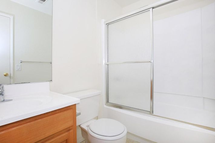 A clean and simple bathroom featuring a shower enclosed in glass, a white bathtub, a toilet, and a wooden vanity with a sink. The walls are painted in a light color, creating a bright and spacious atmosphere. The floor is tiled, and a large mirror is above the sink.