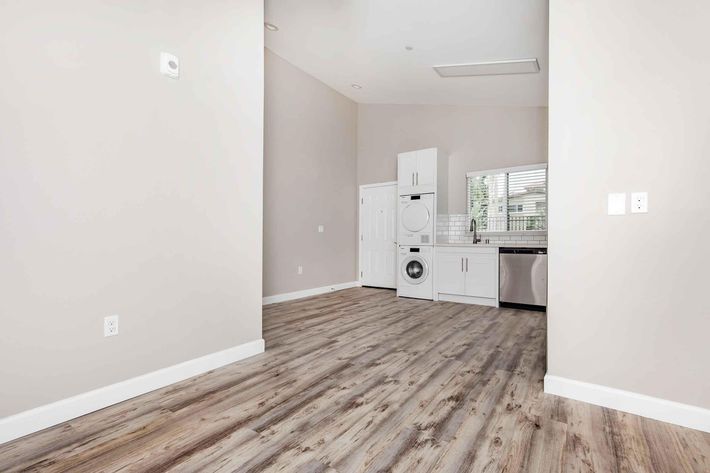 Interior view of a spacious, modern laundry area featuring a washing machine and dryer, with light-colored walls and wooden flooring. A window allows natural light in, creating a bright atmosphere. The room is designed for functionality, with a contemporary aesthetic.