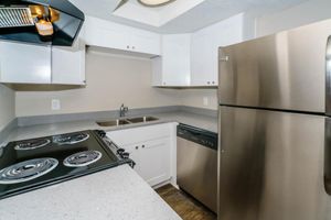Modern kitchen featuring white cabinetry, a stainless steel refrigerator, a dishwasher, and a black electric stove with coil burners. The countertop is light gray with a subtle speckled pattern, and there are double sinks with a chrome faucet. The walls are painted in a neutral tone, creating a bright and inviting space.