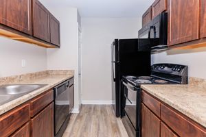 A modern kitchen featuring dark wood cabinetry, granite countertops, stainless steel sink, and black appliances including a refrigerator, microwave, and stove. The flooring is light-colored, and the walls are painted in a neutral tone, creating a spacious and clean look.