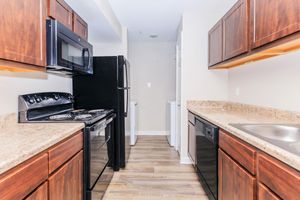 A modern kitchen featuring dark wooden cabinets, a granite countertop, and stainless steel appliances. The layout includes a black refrigerator, a microwave above the stove, an oven with four burners, and a dishwasher next to the sink. The floor is light wood, creating a warm and inviting atmosphere.