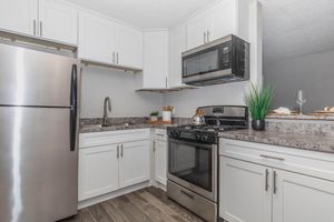 Modern kitchen featuring stainless steel appliances, including a refrigerator and oven, sleek white cabinetry, and a stylish countertop. The space is well-lit with natural light and decorated with potted plants and kitchen utensils. A microwave is mounted above the stove for convenience.