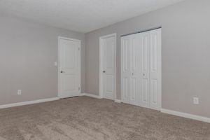 A sparse room featuring light gray walls and plush carpet. There are two closed white doors on the right, one leading to a closet, and an additional door on the left. The space is well-lit and has a simple, clean design, suitable for various uses.