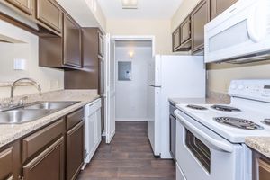 Modern kitchen featuring dark wood cabinets, a double sink, a white refrigerator, and a white microwave above a smooth-top stove. The countertops are granite, and the flooring is dark wood laminate. The space is well-lit with a light fixture and has an open layout leading to a nearby room.
