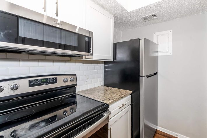 A modern kitchen featuring a stainless steel microwave, black refrigerator, and a sleek, dark-colored oven and stovetop. The countertops are made of light-colored granite, and the walls are painted in a soft gray. The cabinetry is white with a clean, contemporary design.