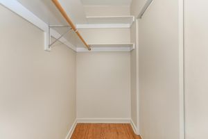 Empty closet with beige walls, a wooden floor, and a wooden clothes rod mounted on the ceiling. Two shelves are installed above the rod, providing storage space. The closet appears spacious and well-lit.