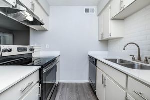 A modern kitchen featuring stainless steel appliances, including a gas range, dishwasher, and double sink. The cabinets are light-colored, with a white backsplash and a sleek countertop. The flooring is a light wood laminate, and the walls are painted in a neutral tone.