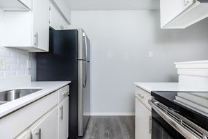 A modern kitchen featuring white cabinets, a stainless steel refrigerator, a silver stove, and a sink. The countertops are light-colored, with a clean and minimalistic design. The walls are painted in a soft gray, creating a bright and airy atmosphere.