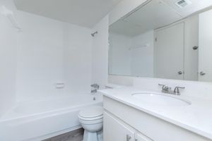 A clean, modern bathroom featuring a white bathtub, sink with a marble countertop, and a large mirror above the sink. The walls and flooring are light-colored, accented by simple fixtures. A door leads to another space, and there's a towel rack installed on the wall.