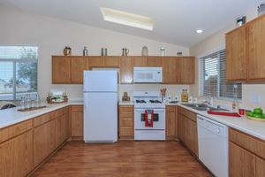 Bright, airy kitchen with wooden cabinets, white appliances including a refrigerator and microwave, and a dishwasher. The countertops are clear, showcasing a few decorative items. Natural light streams in through the windows, and there are green apples placed on the counter for a fresh touch.