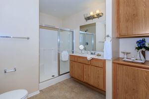 Modern bathroom featuring a glass shower, wooden cabinetry, a sink with a mirror, and a decorative arrangement of flowers. The walls are light-colored, and the floor is tiled, creating a clean and spacious feel. Hand towels are neatly displayed, adding to the overall organized appearance.