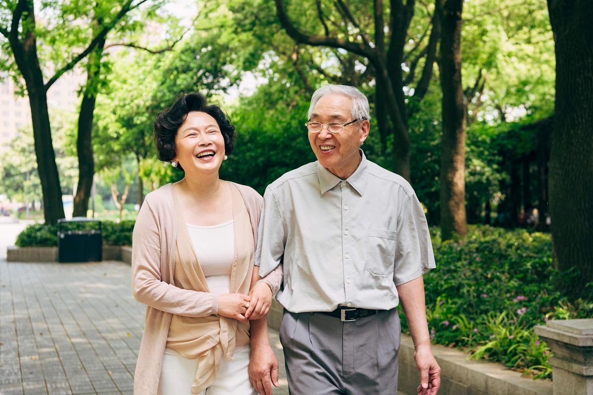 Senior-Asian-Couple-Walking-Trees-1160979740.jpg