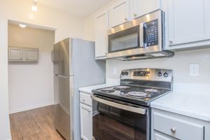 Modern kitchen featuring stainless steel appliances, including a refrigerator, microwave, and an electric range with a smooth countertop. Light-colored cabinetry and a neutral wall color create a bright and inviting atmosphere. The flooring is a warm wood tone, adding to the contemporary design.